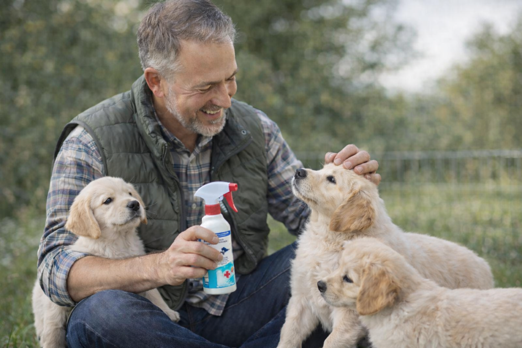 Éleveur de chiens assis en extérieur avec plusieurs chiots, tenant un produit vétérinaire d’hygiène adapté à l’élevage canin.